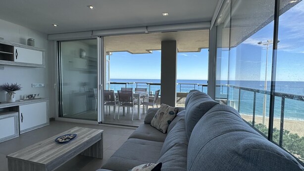 Un salon moderne avec un canapé gris, une table basse en bois et une porte coulissante en verre donnant sur un balcon avec vue sur l’océan.