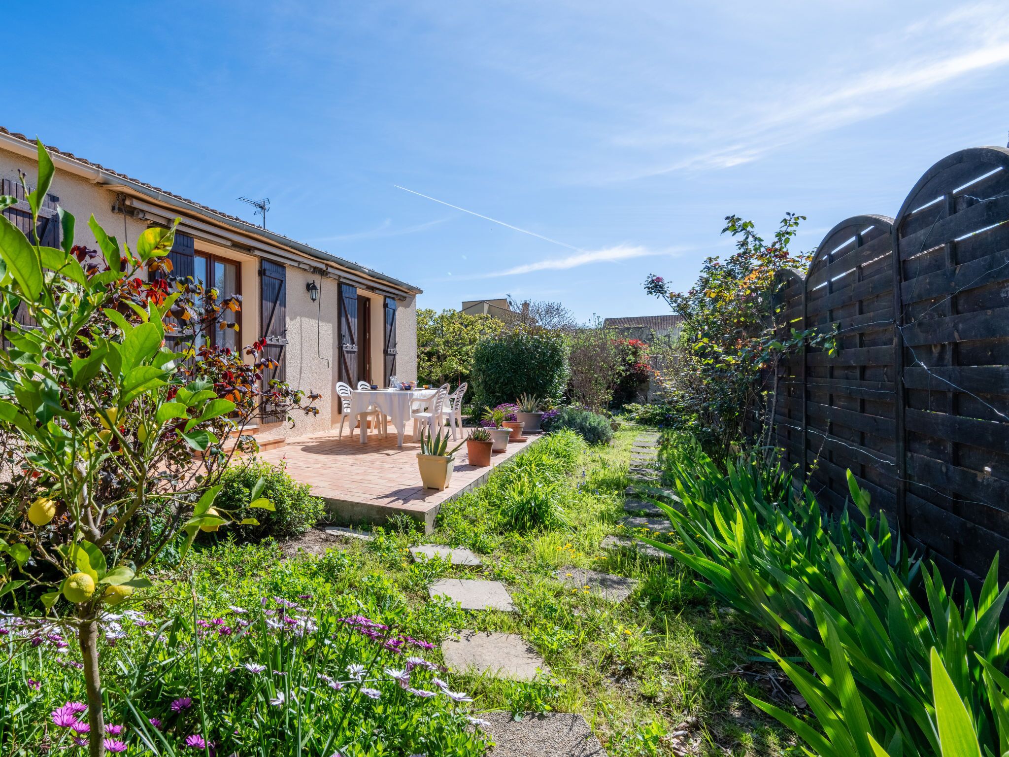 A garden with a patio table and chairs, surrounded by lush greenery and flowering plants.