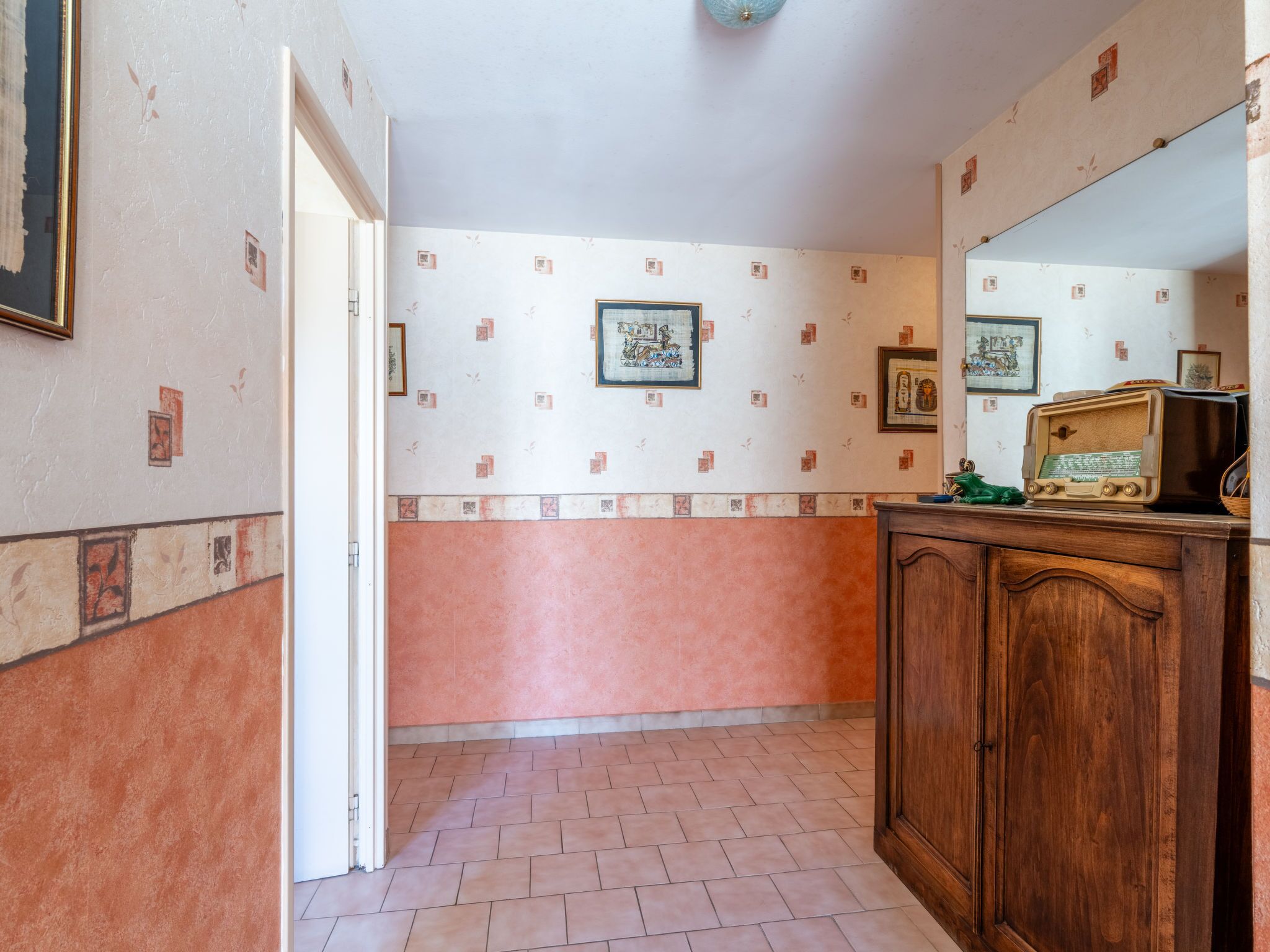 Un couloir doté d’un sol carrelé, d’une armoire en bois et d’un mur orné de tableaux encadrés.
