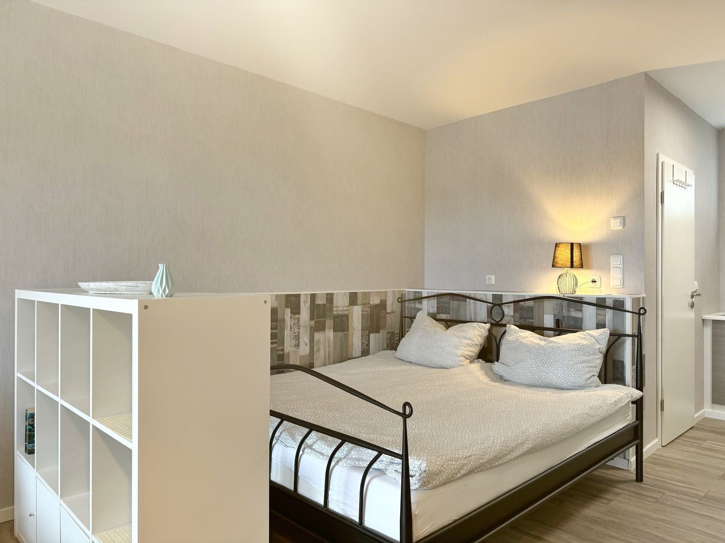 A bedroom with a bed, a bedside table, a lamp, and a wardrobe.
