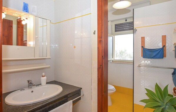 Un baño con lavamanos blanco, espejo y zona de ducha con puerta de cristal.