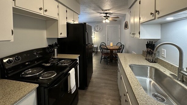 A compact kitchen with white cabinets, a black stove, a sink, and a dining area with a table and chairs.