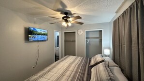 A bedroom with a bed, a ceiling fan, a TV mounted on the wall, and a closet.