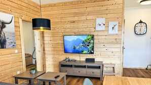 Una habitación acogedora con paneles de madera, un televisor de pantalla plana, un sofá, una mesa de comedor y un reloj en la pared.