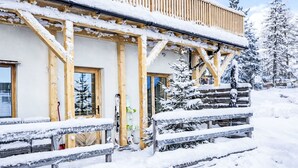 Una cabaña de madera con balcón, escalones cubiertos de nieve y un soporte para esquíes en el exterior.