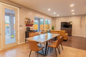 Un vaste espace de vie comprenant une table à manger, des sièges confortables, un téléviseur à écran plat et une porte-fenêtre coulissante donnant sur un patio extérieur.