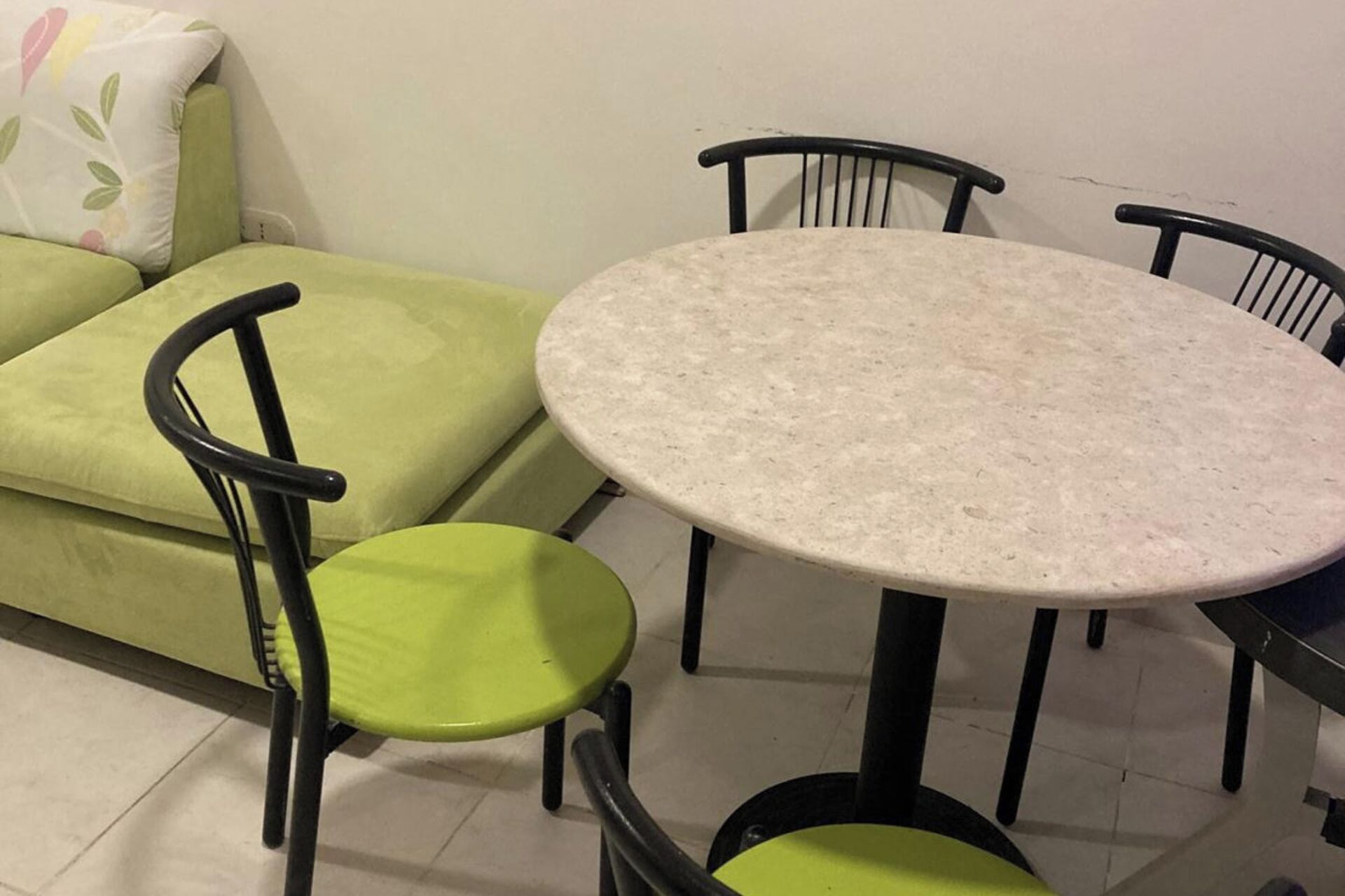 A small, round table with four chairs, a green sofa, and a white wall.