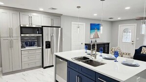 Una cocina moderna con electrodomésticos de acero inoxidable, una encimera blanca y un comedor con cristalería azul.