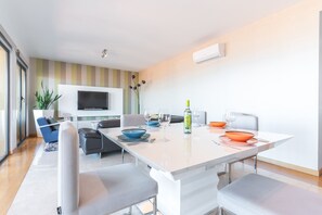 A modern dining area with a white table, grey chairs, and a flat-screen TV mounted on the wall.