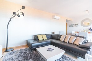 A modern living room with a black leather sofa, a white coffee table, a floor lamp, and a ring light.