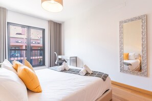 A hotel room with a bed, a desk, a chair, a large window, and a mirror.
