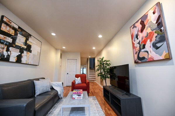 A modern living room with a black leather sofa, a red armchair, a coffee table with a box, a TV on a stand, and abstract paintings on the walls.