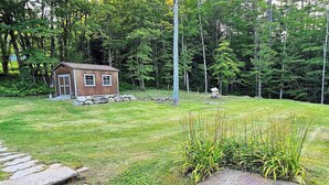 Une petite cabane en bois, entourée d’un paysage verdoyant luxuriant, avec un sentier de pierres qui y mène.