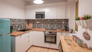Una cucina moderna con mobili bianchi, un forno a microonde, un forno e un lavandino. C'è un piano di lavoro in legno e un lampadario.