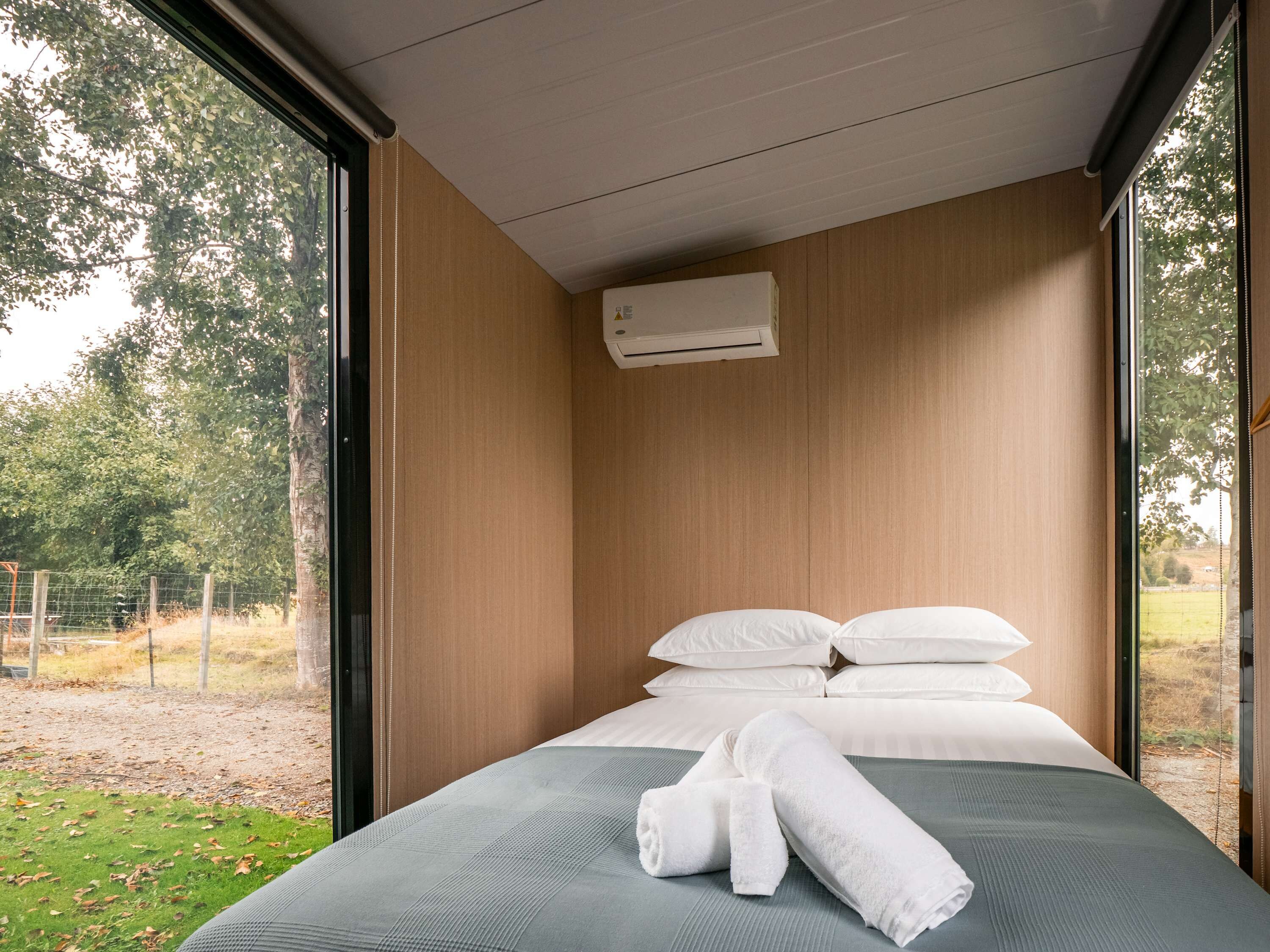Een moderne hotelkamer met een groot bed, witte lakens en uitzicht op een grasveld door grote ramen.