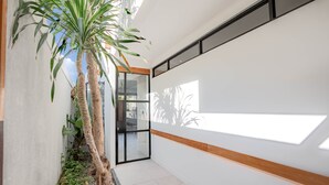 A modern interior with a white wall, a wooden accent strip, and a glass door leading to an outdoor area. - Town House Camy Bali (Bali)