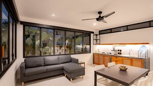 A modern kitchen with a large window, a gray sectional sofa, and a dining table with chairs. - Town House Camy Bali (Bali)