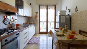 A compact kitchen with a gas stove, oven, and a refrigerator. There is a dining table with a floral tablecloth and orange cups. - Garden an Seaview by Interhome (Laigueglia)