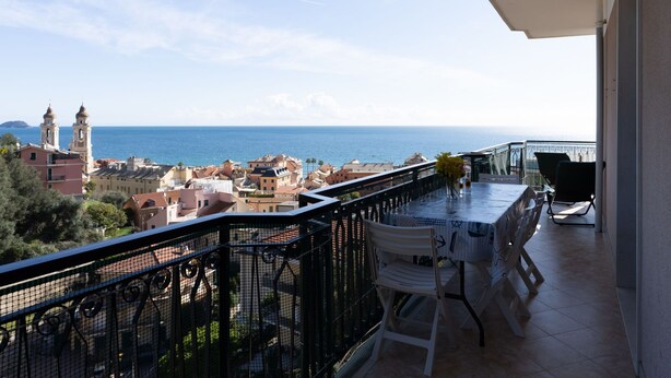 A balcony with a table and chairs, overlooking a coastal town with buildings and a clear sky. - Garden an Seaview by Interhome (Laigueglia)