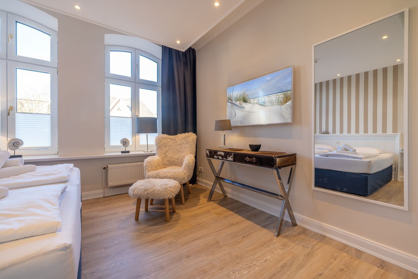 A bedroom with a bed, a chair, a desk, a painting, and a mirror.