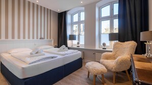 Et hotelværelse med en seng, en stol, et bord og et vindue med gardiner.