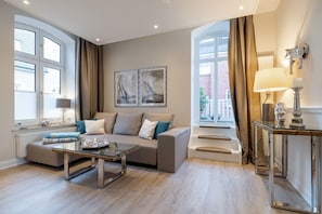 Un salon moderne avec un canapé, une table basse en verre et un escalier menant à un balcon.