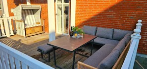 A deck with a wooden table, a cushioned bench, and a wicker chair.
