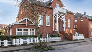En murstensbygning i rødt med et hvidt stakerværk, en balkon og en trappe til indgangen.