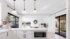 A modern kitchen with white cabinetry, a built-in microwave, pendant lighting, and a large window providing natural light. - Desert Haven: Elegant 3BR/3BA in Indian Wells (Indian Wells)