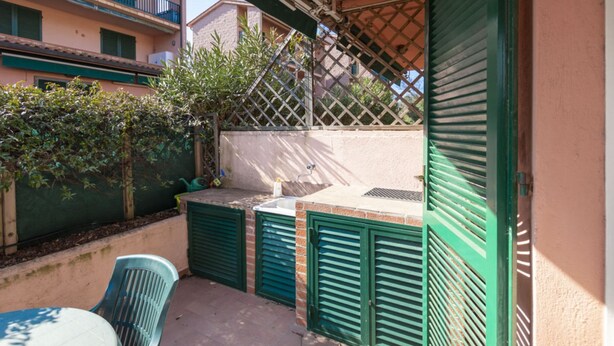 A small outdoor patio with a table and chairs, a green fence, and a view of neighboring buildings. - Two-room apartment Lina, ground floor with fenced outdoor space near the center of Marina di Campo (Campo nell'Elba)