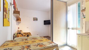 A room with a dining table, chairs, a TV mounted on the wall, and a sliding glass door leading to an outdoor area. - Two-room apartment Lina, ground floor with fenced outdoor space near the center of Marina di Campo (Campo nell'Elba)