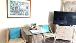 Una sala de estar con muebles de mimbre, una mesa de centro de vidrio, un televisor de pantalla plana y un cuadro en la pared.