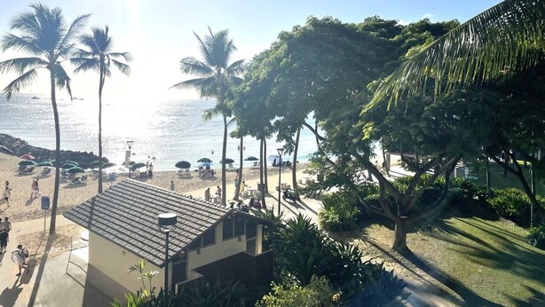 Una playa con palmeras, sombrillas y un edificio de techo inclinado.