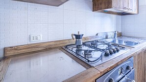 A kitchen with a gas stove, wooden cabinets, a stainless steel sink, and a white tiled backsplash.