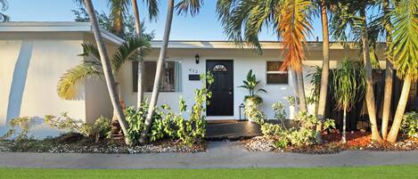 A modern house with a black door, number 612, surrounded by palm trees and well-maintained lawn.