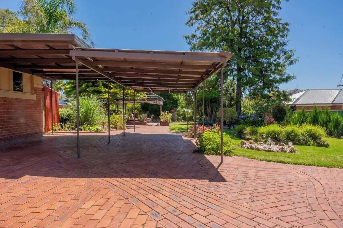 Un espace extérieur abrité, doté d’un chemin en briques, d’une pergola et entouré de verdure.