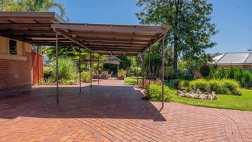 Un espace extérieur abrité, doté d’un chemin en briques, d’une pergola et entouré de verdure.