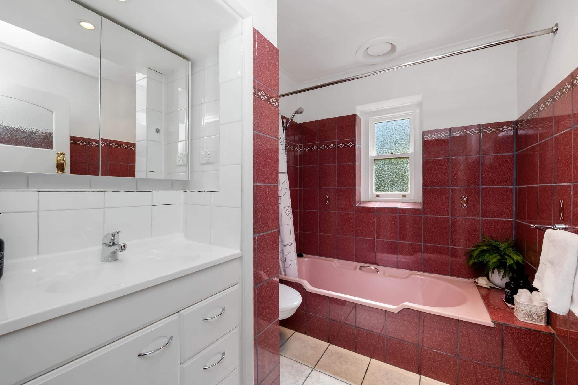 Une salle de bain avec un lavabo blanc, un miroir, une baignoire et une fenêtre.