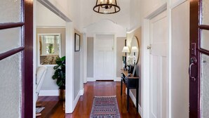 Un couloir doté d’un plancher en bois, d’un tapis à motifs, d’un luminaire suspendu et d’une porte avec un miroir et une petite table.