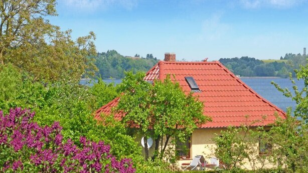 Ein Haus mit rotem Dach, umgeben von üppigem Grün und einem See im Hintergrund.