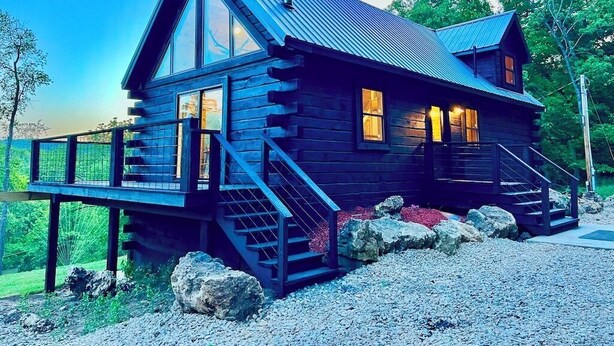 A log cabin with a large front porch, a staircase, and a deck.