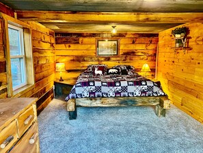 Un dormitorio rústico de madera con una cama, dos lámparas de noche, una ventana y un cuadro en la pared.