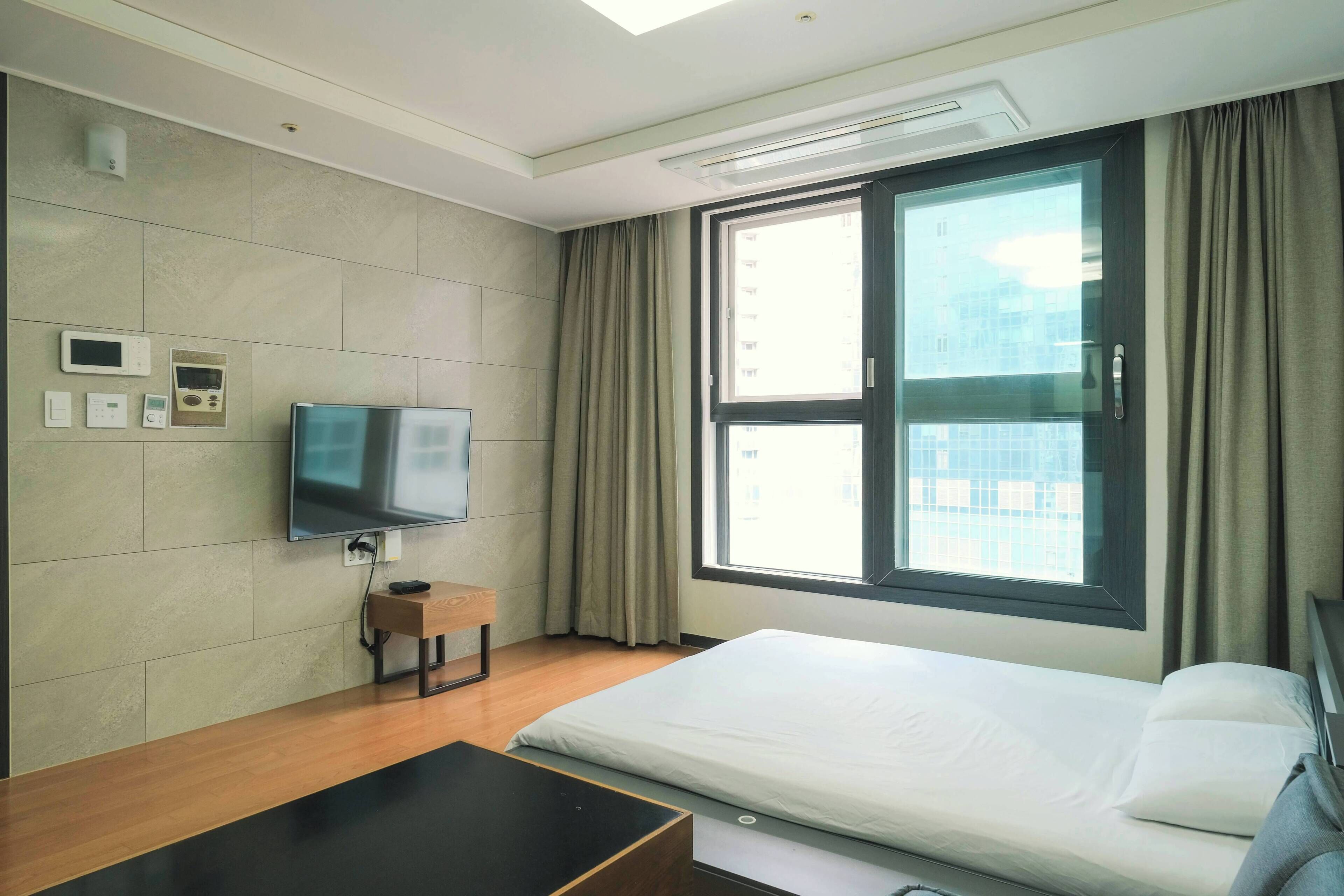 Una habitación de hotel moderna con cama, televisor, escritorio y ventana con cortinas.