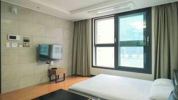 Una habitación de hotel moderna con cama, televisor, escritorio y ventana con cortinas.