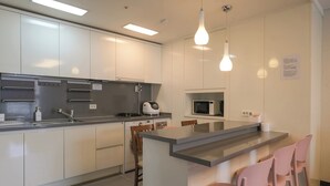 Una cocina moderna con armarios blancos, microondas integrado y una isla central con sillas rosadas.