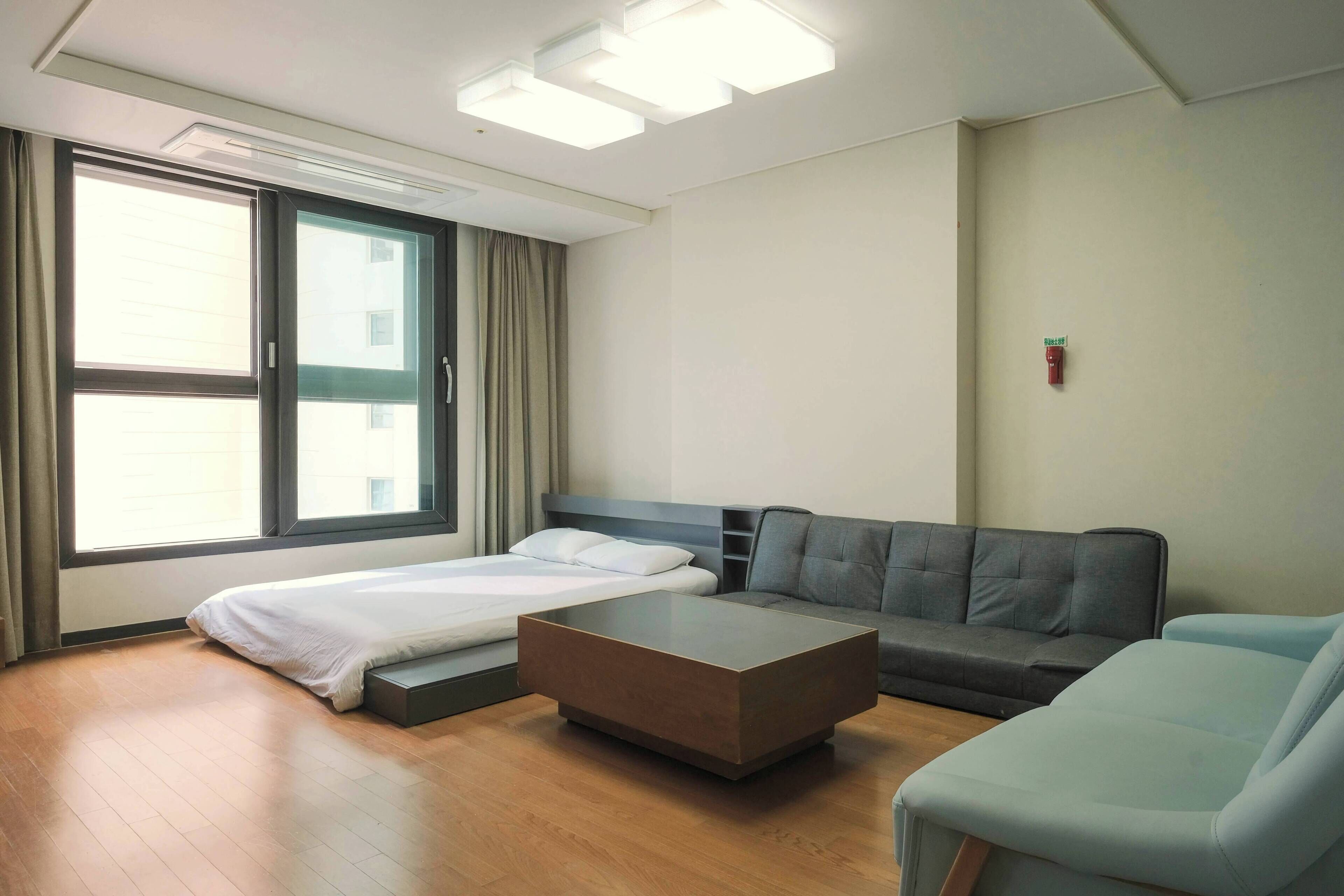 A modern hotel room with a bed, a sofa, a coffee table, and a large window.