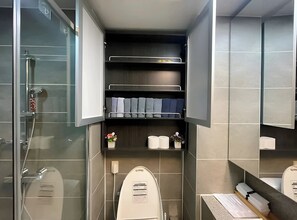 Uma casa de banho moderna com cabine de duche em vidro, sanita com painel de comando e zona de lavatório com bancada.