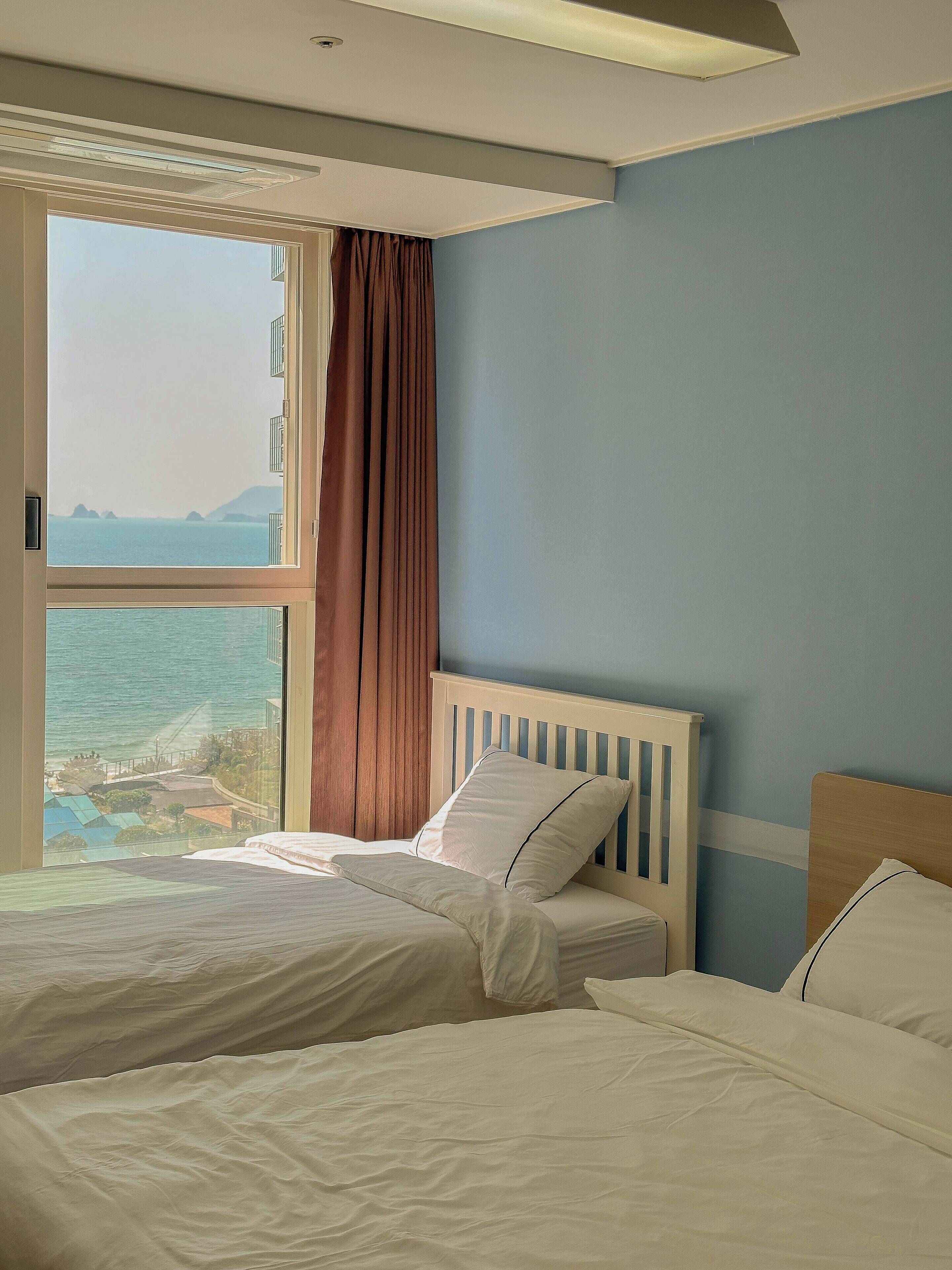Een slaapkamer met twee bedden, uitzicht op zee en een raam met gordijnen.