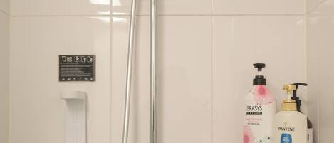 Une douche équipée d’un pommeau de douche à main, d’une étagère en verre pour les articles de toilette et d’un distributeur de serviettes blanches.