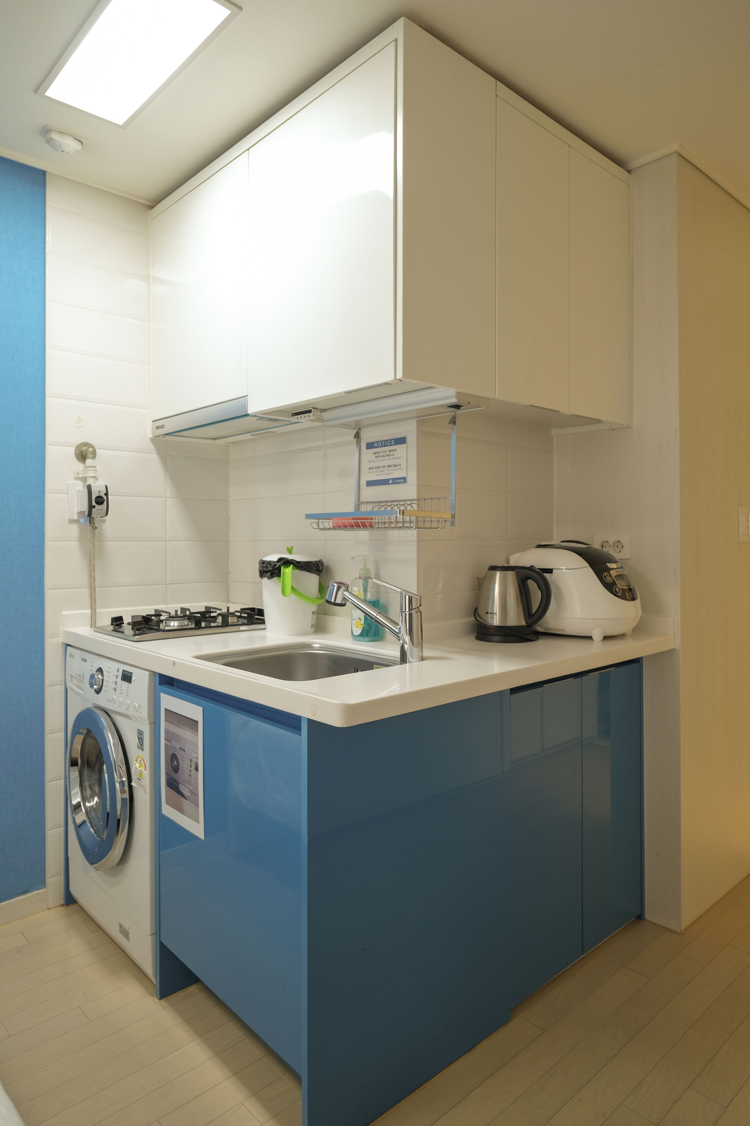 A compact kitchen with a washing machine, a coffee maker, and a kettle on the counter.